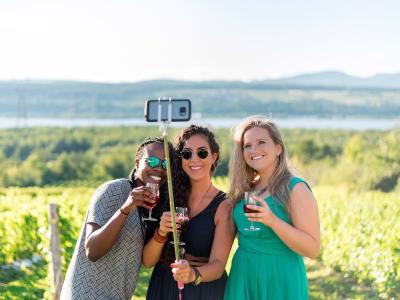 Trois filles souriantes se prennent en photo et prennent un verre au milieu d'un vignoble à l'lle d'Orleans, en été.