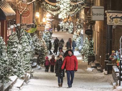 Plusieurs personnes se promènent en soirée sur la rue du Petit-Champlain enneigée et décorée de nombreux sapins illuminés. 