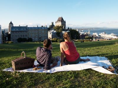 Pique-nique en couple près de la terrasse Pierre-Dugua-De Mons en admirant le Château Frontenac et le fleuve Saint-Laurent. 