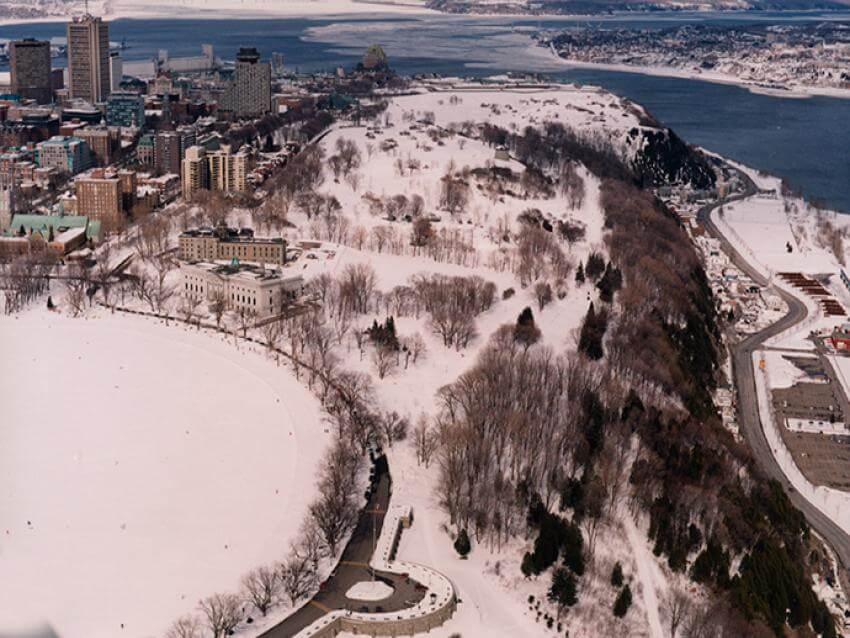 Commission des champs de bataille nationaux - Vue aérienne des plaines d'Abraham en hiver avec le Vieux-Québec et le fleuve Saint-Laurent en arrière-plan.