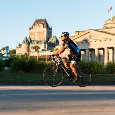 A cyclist rides on a bike path in the Old Port of Québec with the Château Frontenac in the background.