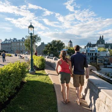 Un couple marche sur la terrasse Pierre-Dugua-De Mons près de l'avenue Saint-Denis, en regardant le Château Frontenac.